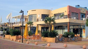 Un immeuble avec un restaurant au rez-de-chaussée, une terrasse avec des parasols et un vélo garé à l’extérieur.