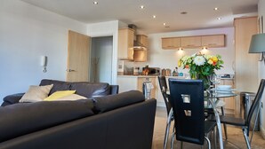 A modern living room with a black leather sofa, a dining table with chairs, and a kitchen area in the background. - Clarence Court - Free Parking, W-Fi & Netflix (Newcastle)