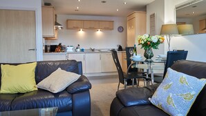 A modern living room with a black leather sofa, a glass coffee table, and a dining area with a glass table and chairs. - Clarence Court - Free Parking, W-Fi & Netflix (Newcastle)
