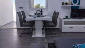Un salon moderne avec un coin repas, un téléviseur posé sur un meuble blanc et une fenêtre donnant sur des arbres.