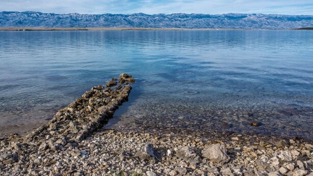 Un lac paisible, bordé d’une rive rocheuse, avec des montagnes en arrière-plan.