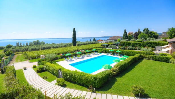 Une piscine entourée de pelouses et de haies parfaitement entretenues, offrant une vue dégagée sur la mer en arrière-plan.