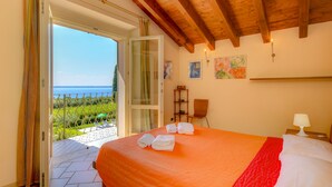 Une chambre avec une couvre-lit orange, un plafond en bois et une vue sur la mer par une porte ouverte.