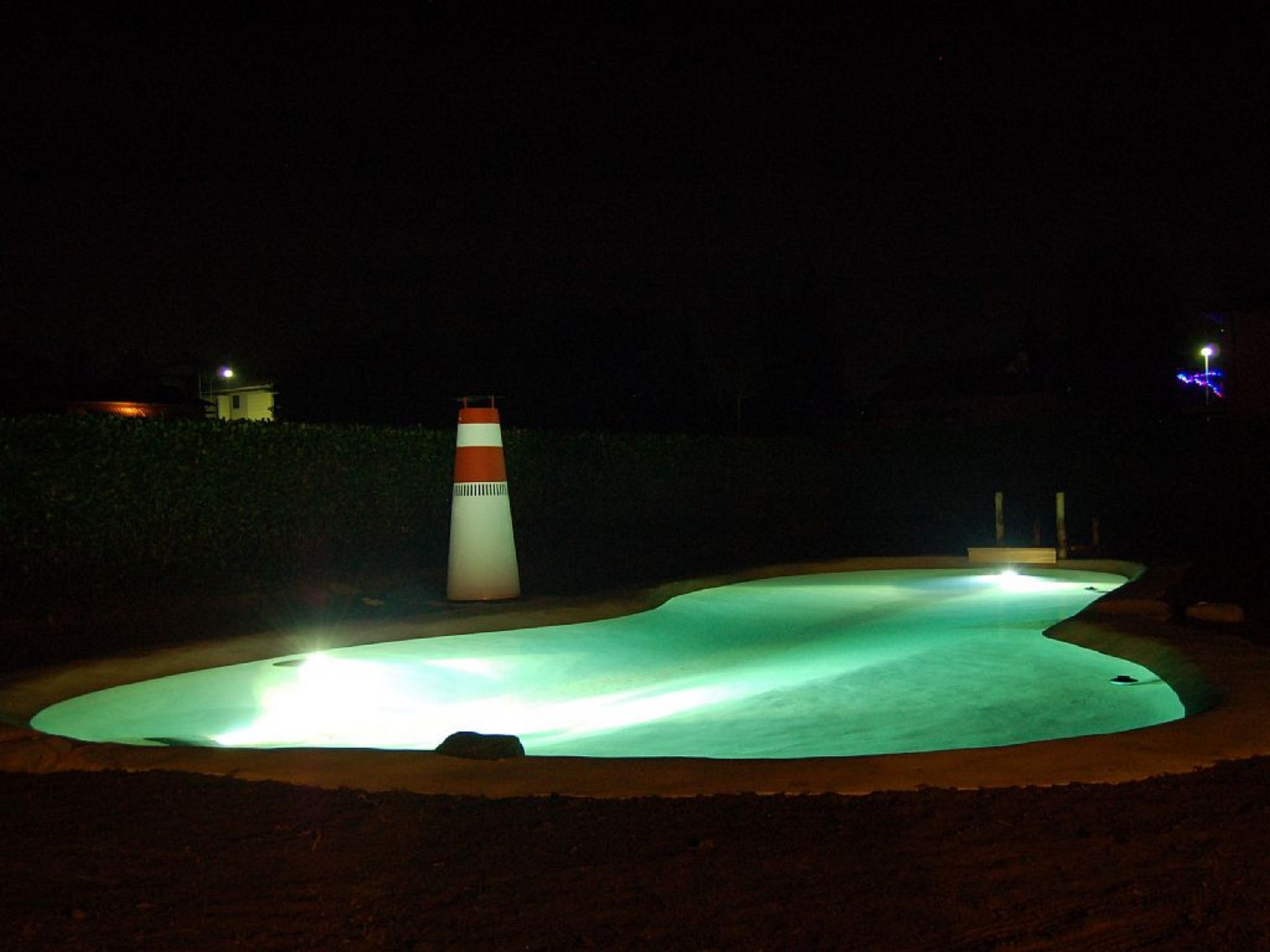 A swimming pool at night with a lighthouse-like structure in the background.