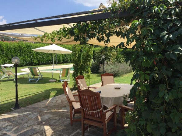 A patio with a round table and chairs, surrounded by greenery and a pergola. - Betulla, Barga! Private beach style pool, WIFI, walk to bars/restaurants! (Barga)