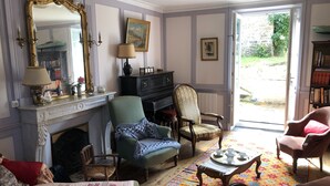 A traditional living room with a fireplace, a large mirror, and a view of the garden through an open door. - House with garden (Saint-Malo)