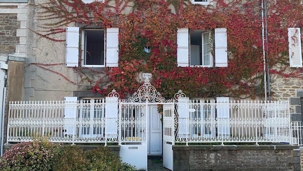A stone building with ivy-covered walls, white shutters, and a white wrought iron gate. - House with garden (Saint-Malo)