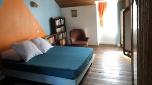A bedroom with a bed, a bookshelf, a chair, and a window with curtains. - House with garden (Saint-Malo)