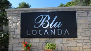 Señal de 'Blu Locanda' con un muro de piedra de fondo y dos plantas en macetas al frente.