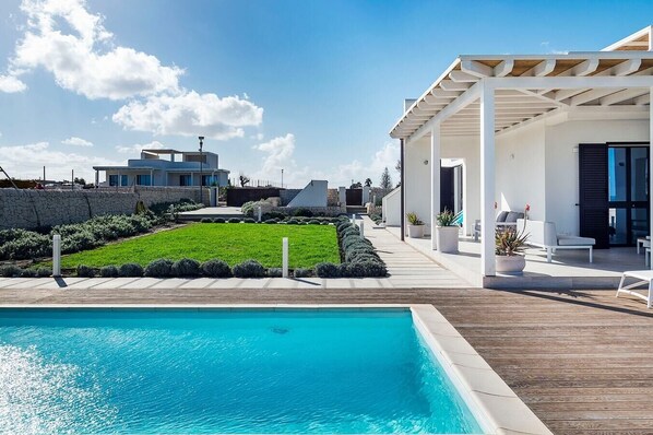 A modern outdoor pool area with a clear blue pool, a well-maintained lawn, and a covered seating area with outdoor furniture.