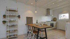 Una cucina moderna con tavolo in legno e sedie bianche, un lampadario a sospensione e un ripiano contenitore bianco con piante.