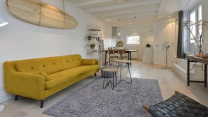 Un soggiorno moderno con un divano giallo, un tavolino rotondo e una tavola da surf appesa al muro.