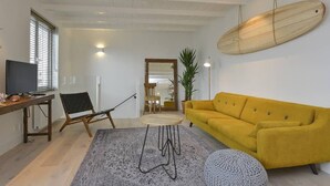 Un soggiorno moderno con un divano giallo, un tavolino rotondo e un televisore su un mobile in legno.
