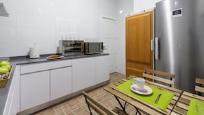 Una cocina moderna con armarios blancos, un refrigerador de acero inoxidable, un microondas y un tostador. Hay una mesa de comedor con un mantel individual verde y una taza.