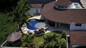 Vue aérienne d’un complexe hôtelier avec une piscine, des chaises longues et un abri à toit de chaume.