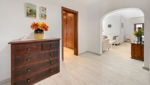 A hallway with a wooden dresser, a vase of flowers, and a door leading to a living area with a white sofa and a small table.