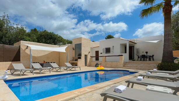 A swimming pool with lounge chairs, a small table with chairs, and a covered area.