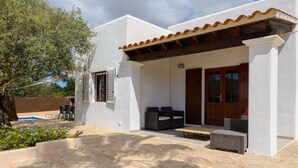 A white building with a covered patio, outdoor seating, and a pool.