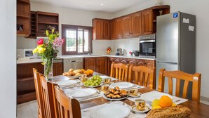 A modern kitchen with wooden cabinets, a stainless steel refrigerator, and a dining table set for breakfast.