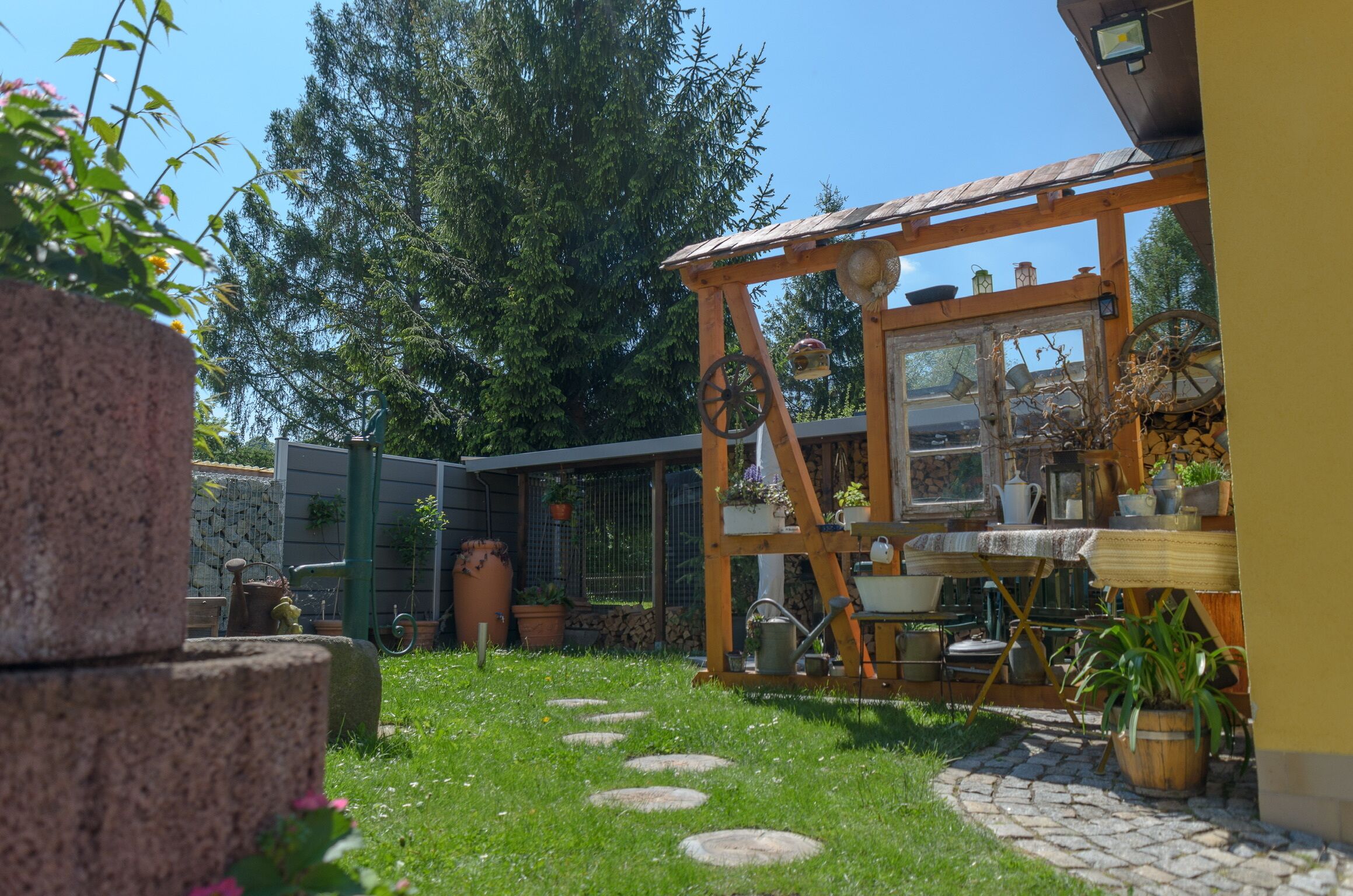 Un'area esterna rustica con una pergola in legno, un vialetto in pietra e diverse piante in vaso.