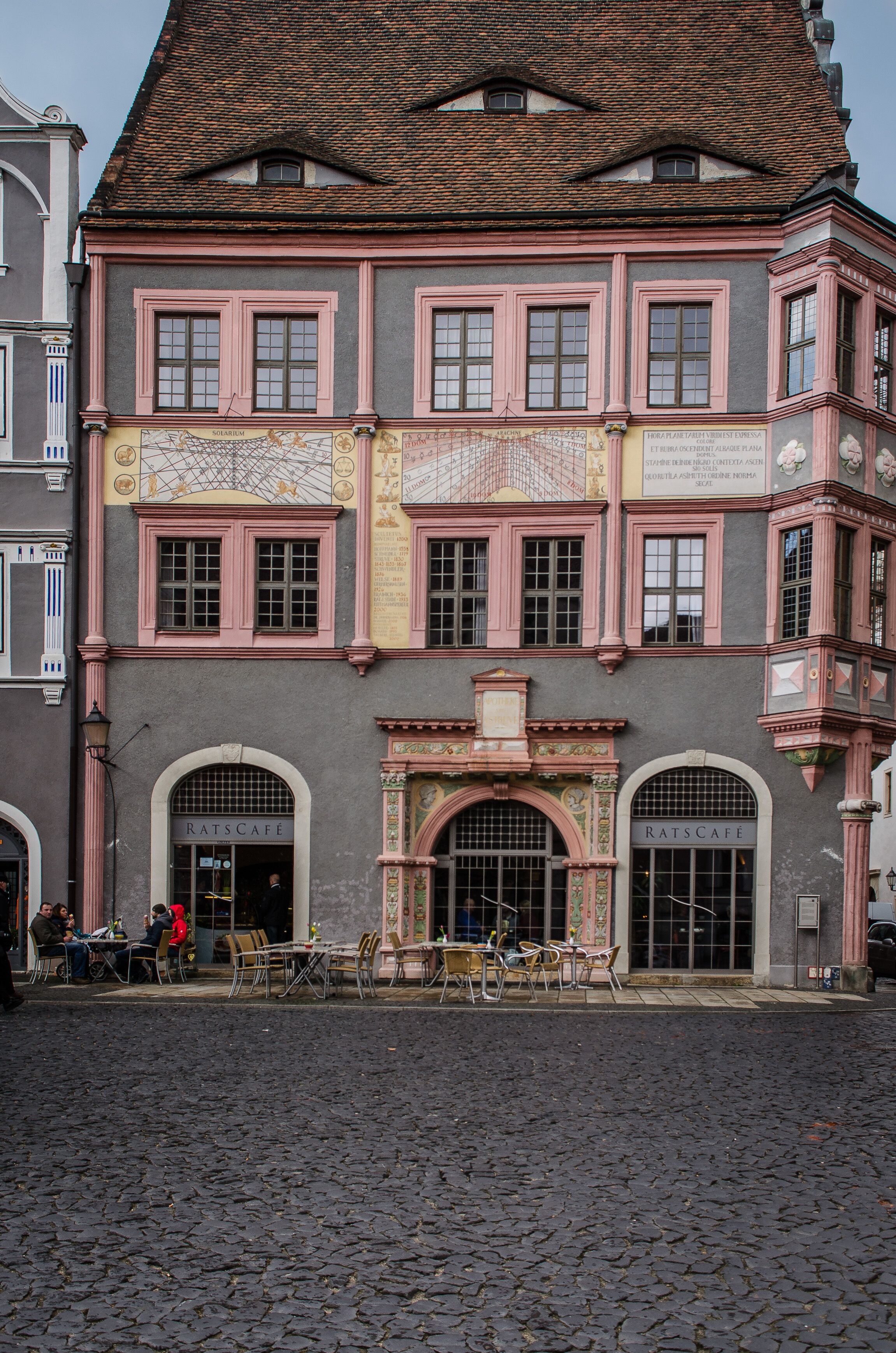 A historic building with a café on the ground floor, featuring traditional architecture and a cobblestone street in front.