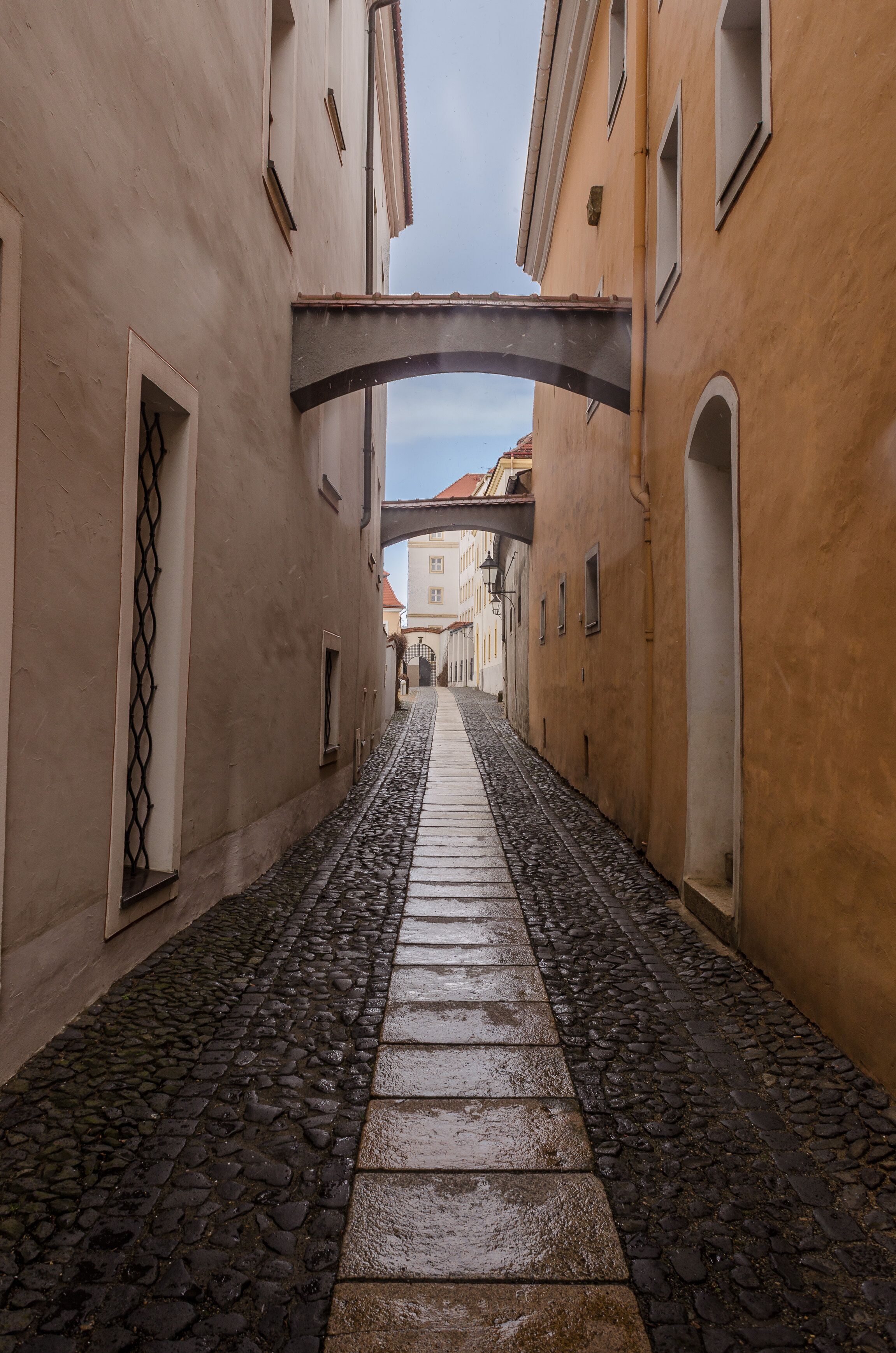 A narrow cobblestone street flanked by buildings with arched windows and doorways.