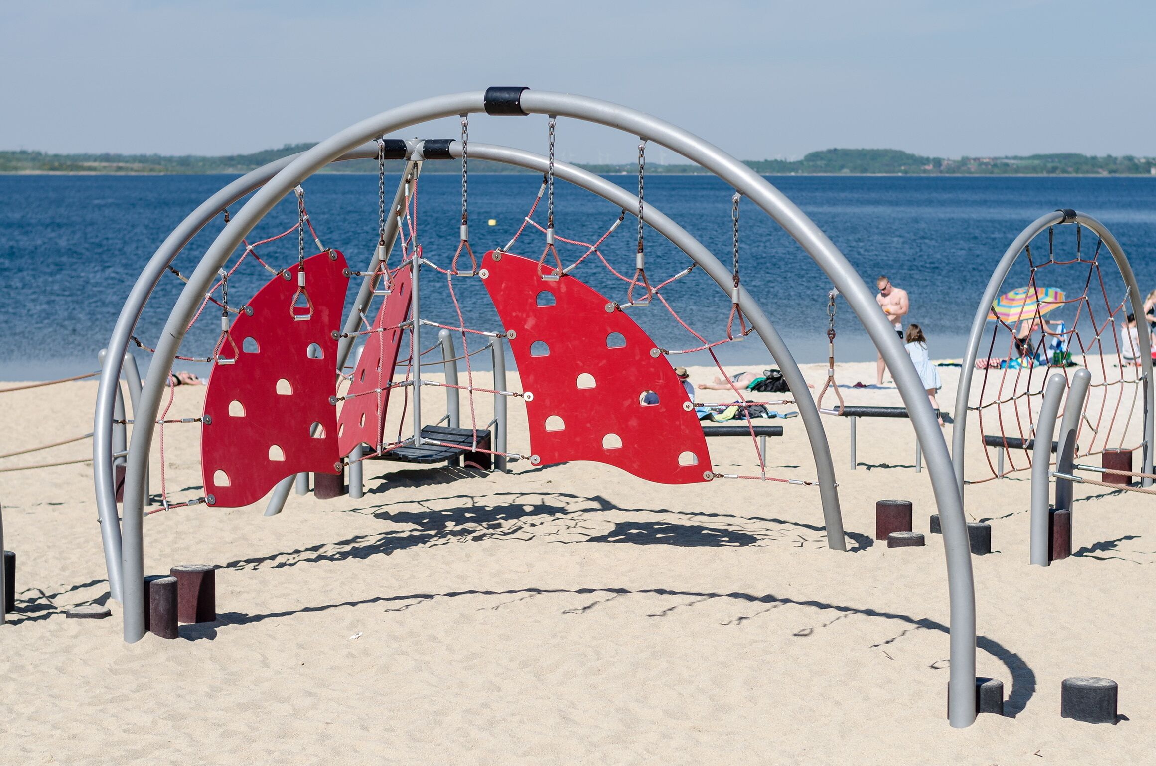 A beach playground with swings and a netted play area.