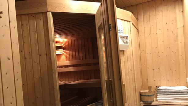 A wooden sauna with a bench, a control panel, and a towel rack.