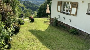 A house with a white exterior, a sloped roof, and a garden with a lawn and potted plants.