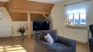 A living room with a high ceiling, a flat-screen TV, a sofa, a chair, a window with curtains, and a decorative deer figurine.