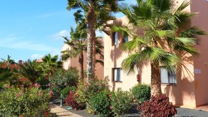 A building with multiple floors, palm trees, and a variety of shrubs and flowers in the surrounding garden area. - Apartment Gardenia, Oasis Tamarindo, seaview, tropical Garden, 2 Pools (La Oliva)