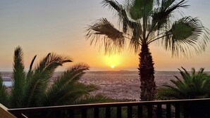 A sunset view from a balcony with palm trees, overlooking a beach. - Apartment Gardenia, Oasis Tamarindo, seaview, tropical Garden, 2 Pools (La Oliva)