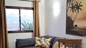 A living room with a sofa, a dining table, and a painting of palm trees. - Apartment Gardenia, Oasis Tamarindo, seaview, tropical Garden, 2 Pools (La Oliva)