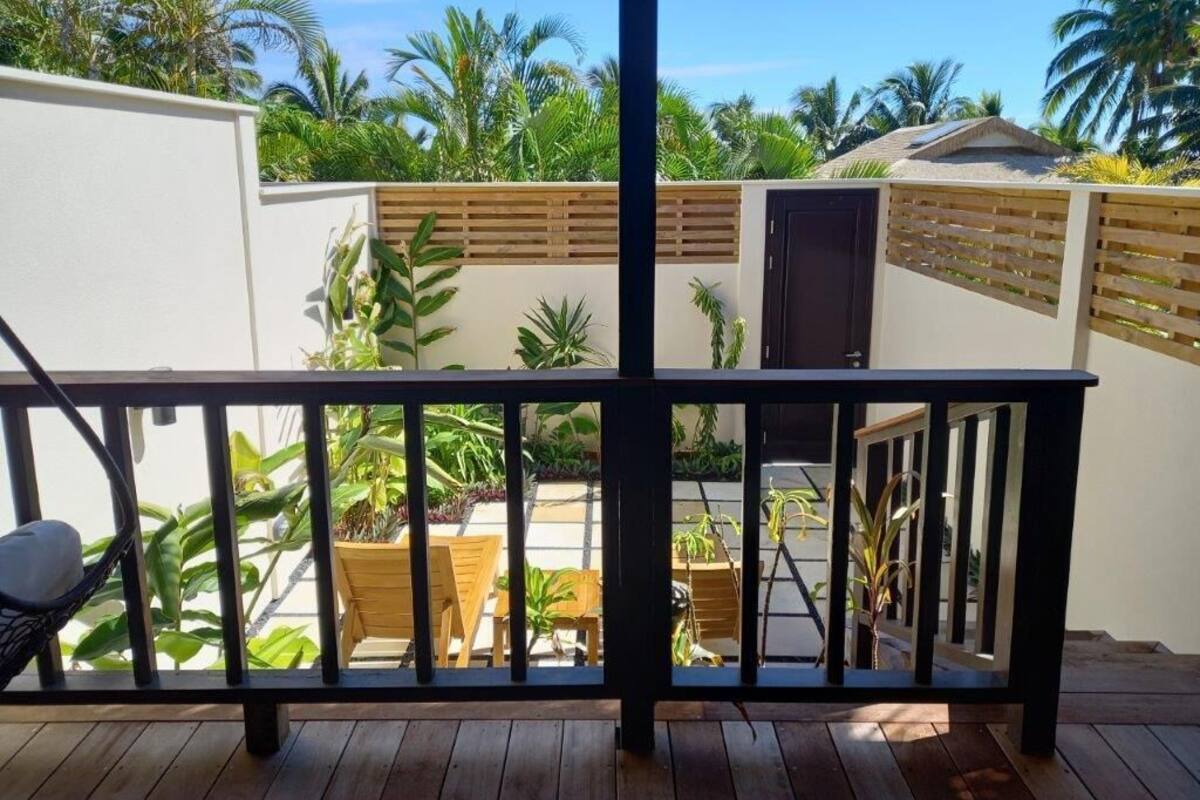 A wooden deck with a black railing, surrounded by lush greenery and palm trees.