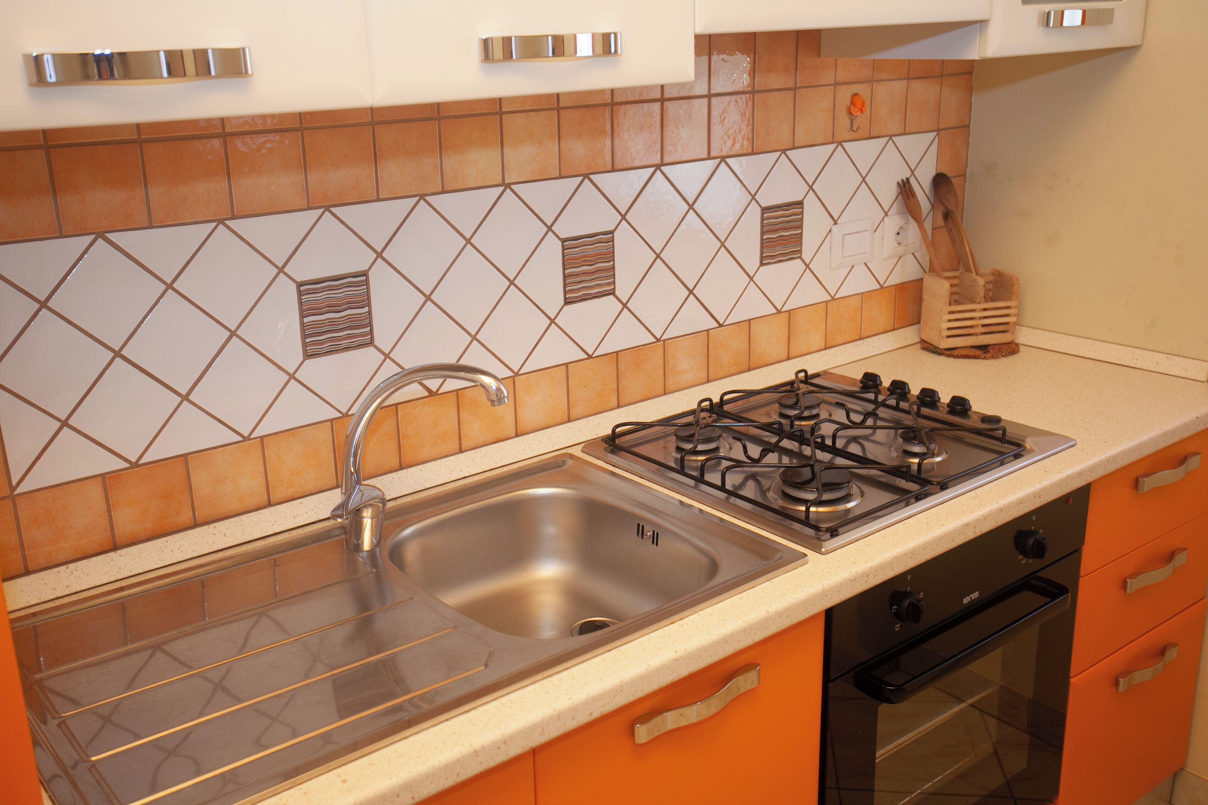 A kitchen with a stainless steel sink, gas stove, oven, and orange cabinets.