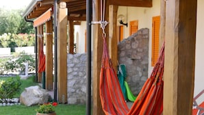A wooden structure with hammocks hanging, a stone wall, and a potted plant on a wooden stump. - villas just by the sea (Santa Maria di Ricadi)
