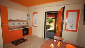 A compact kitchen with orange cabinets, a dining table with chairs, and a view of the outside.