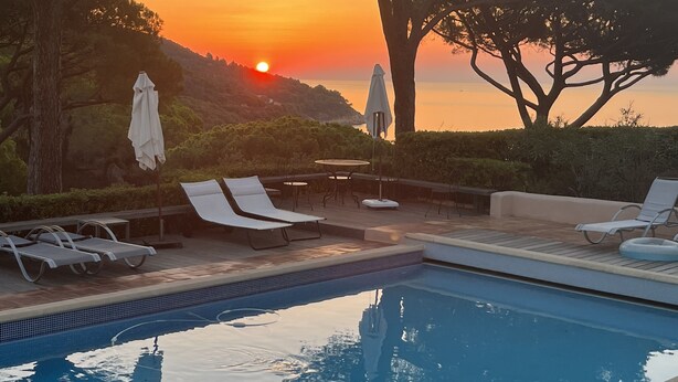 A poolside area with lounge chairs and umbrellas, overlooking a body of water and a sunset. - Exceptional property, panoramic sea views, pool, private tennis court, air-con (Ramatuelle)