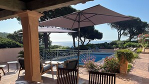 A covered outdoor seating area with a pool, chairs, and umbrellas. - Exceptional property, panoramic sea views, pool, private tennis court, air-con (Ramatuelle)