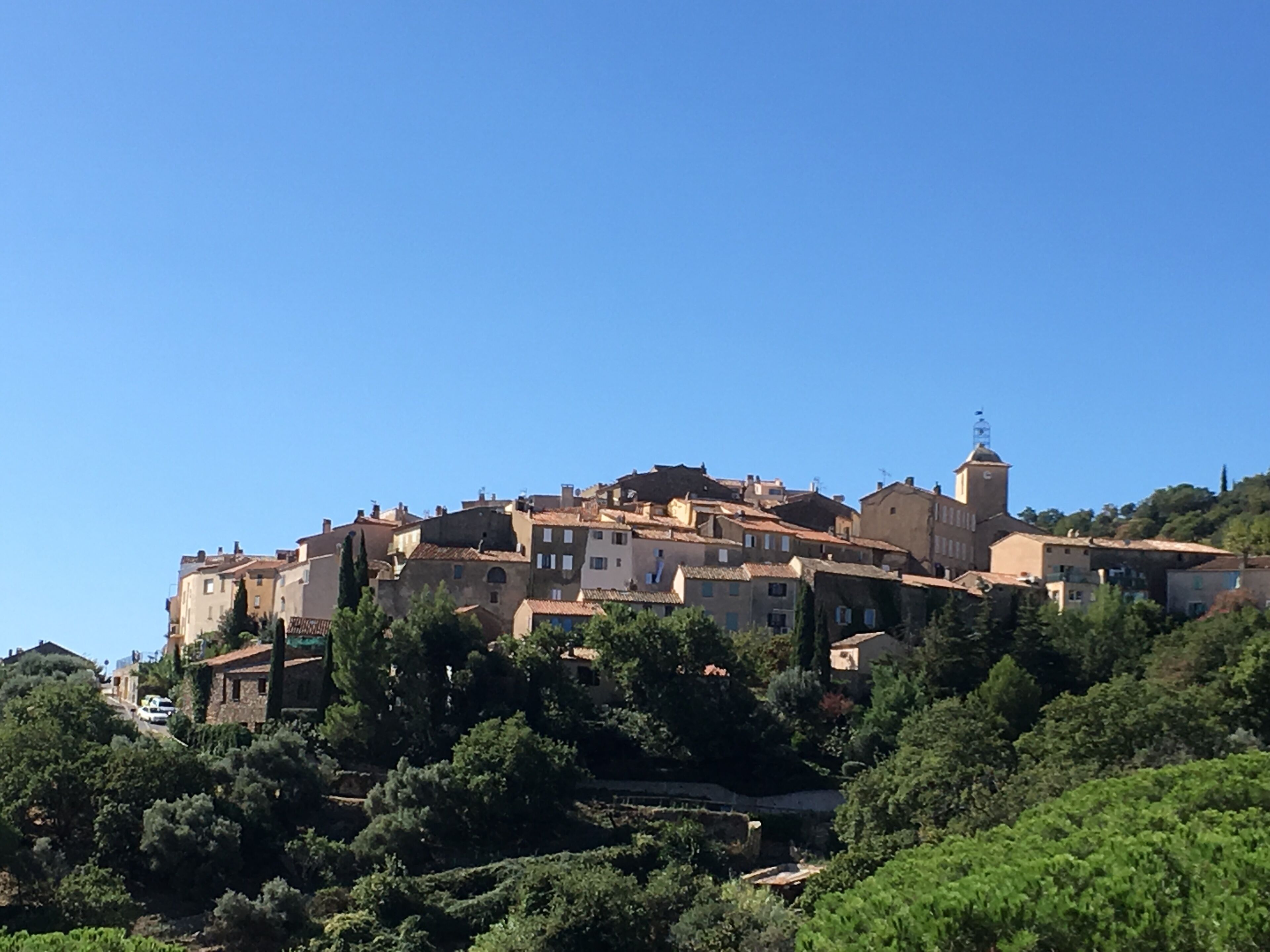 Une ville située sur une colline, avec des bâtiments historiques, une végétation luxuriante et un ciel dégagé.