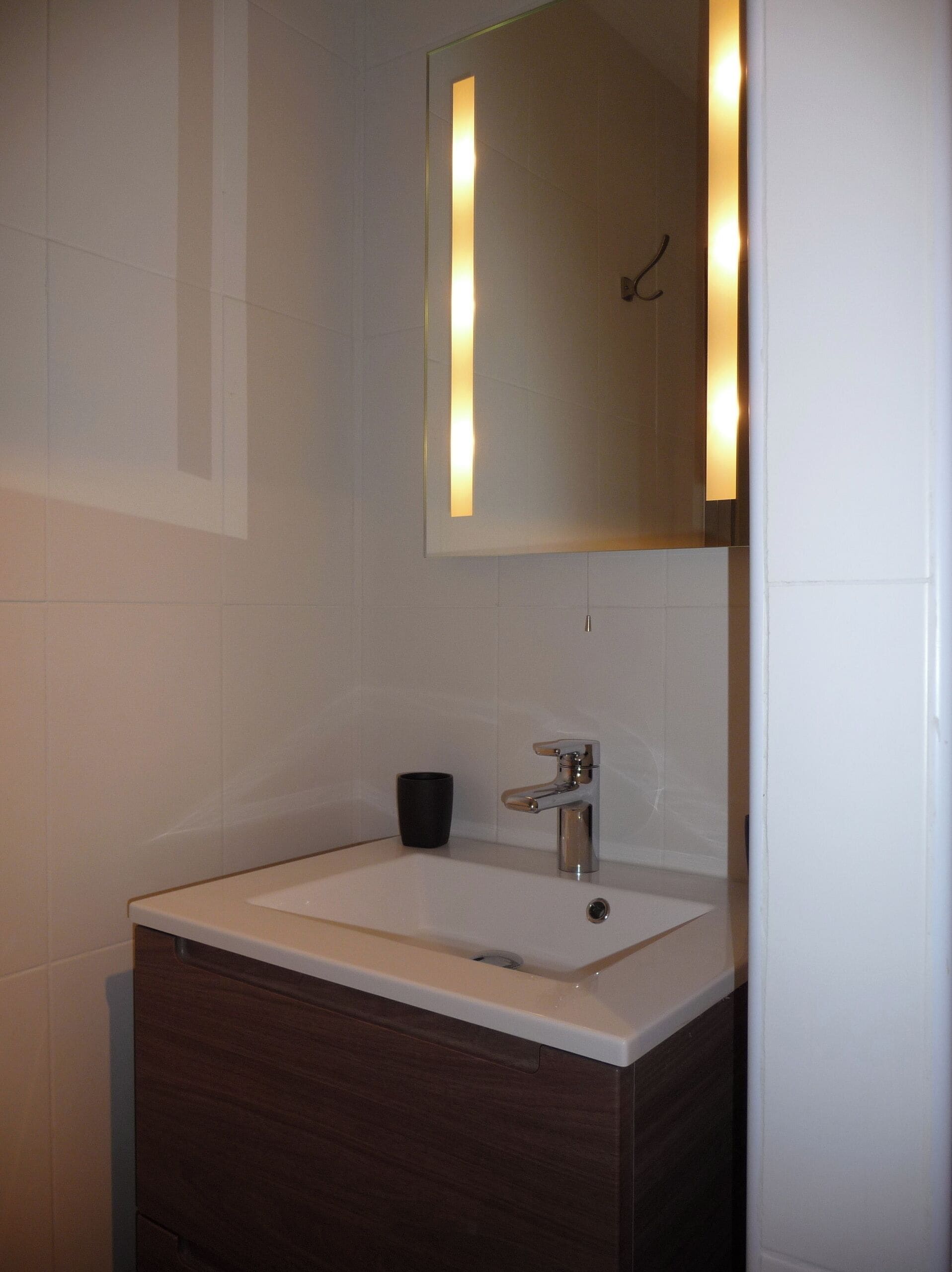 A bathroom with a white sink, dark wooden vanity, and a mirror with vertical light strips.