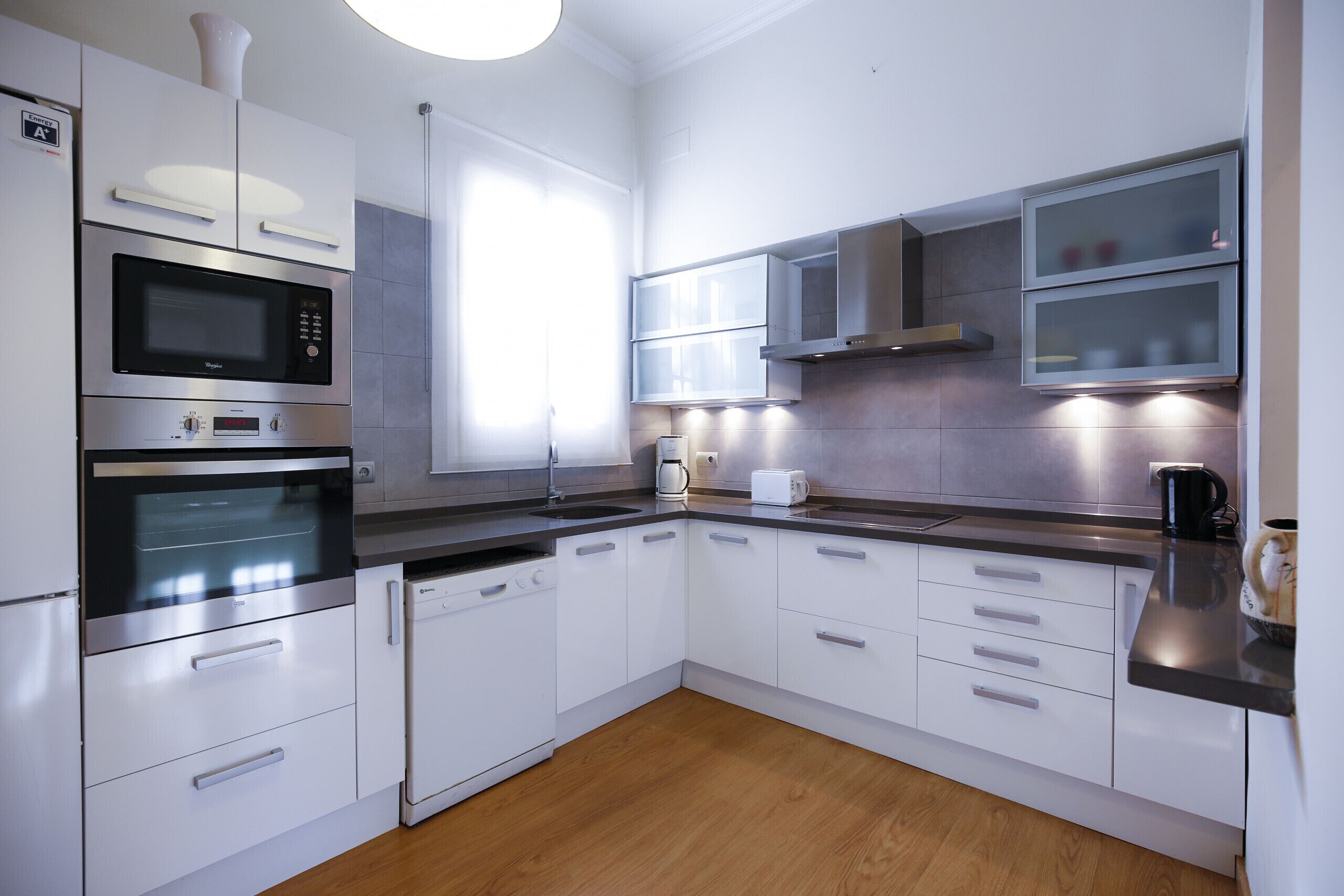 Una cocina moderna con armarios blancos, electrodomésticos de acero inoxidable y piso de madera.