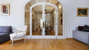 A room with a white leather armchair, a grey sofa, and a glass door leading to a dining area.