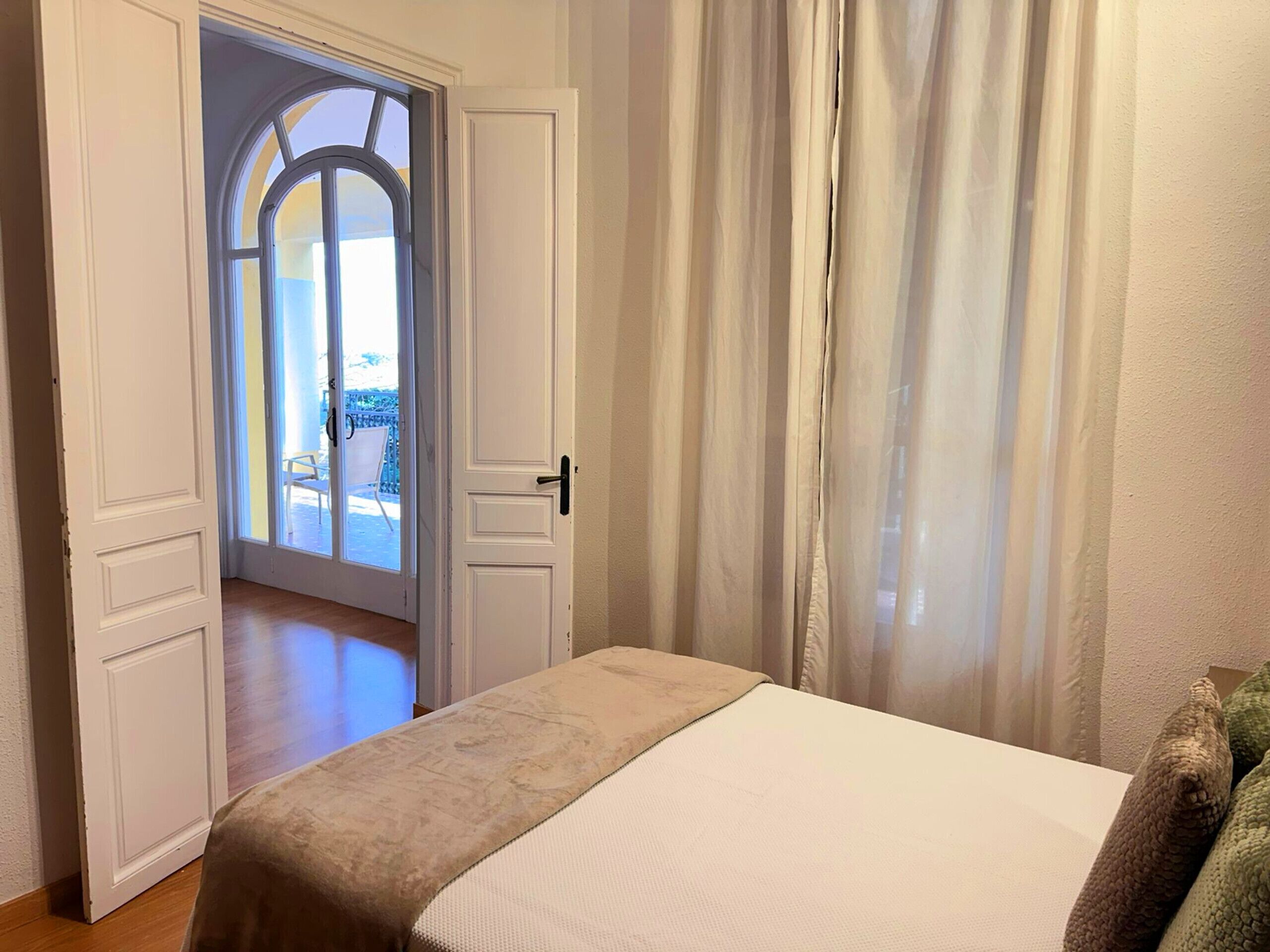 A hotel room with a bed, a door leading to a balcony, and a view of the outdoors.
