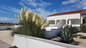 Un edificio moderno con fachada blanca y tejado rojo, rodeado de zonas ajardinadas que incluyen pastos altos y plantas de agave.