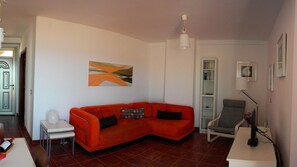 A living room with a red sofa, a white side table, a bookshelf, and a grey armchair. - Modern Oceanfront Penthouse Apartment. Very Spacious. Big Sunbathing Terrace. (El Medano)