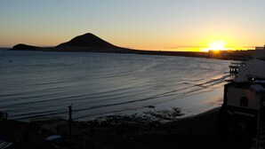 A coastal sunset view with a mountain in the distance and a beach with a pier. - Modern Oceanfront Penthouse Apartment. Very Spacious. Big Sunbathing Terrace. (El Medano)