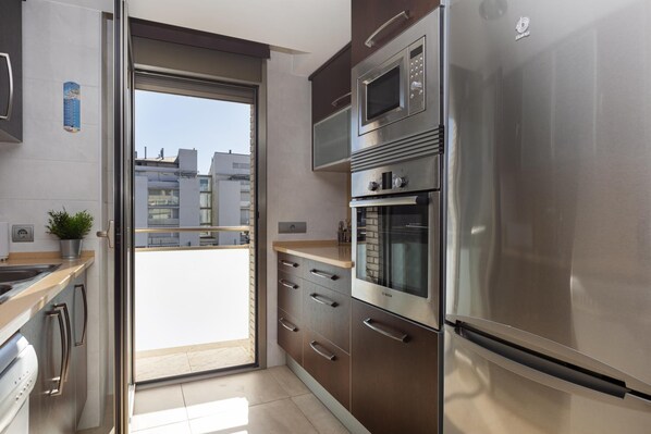 A modern kitchen with stainless steel appliances, a sliding door to a balcony, and a view of buildings.