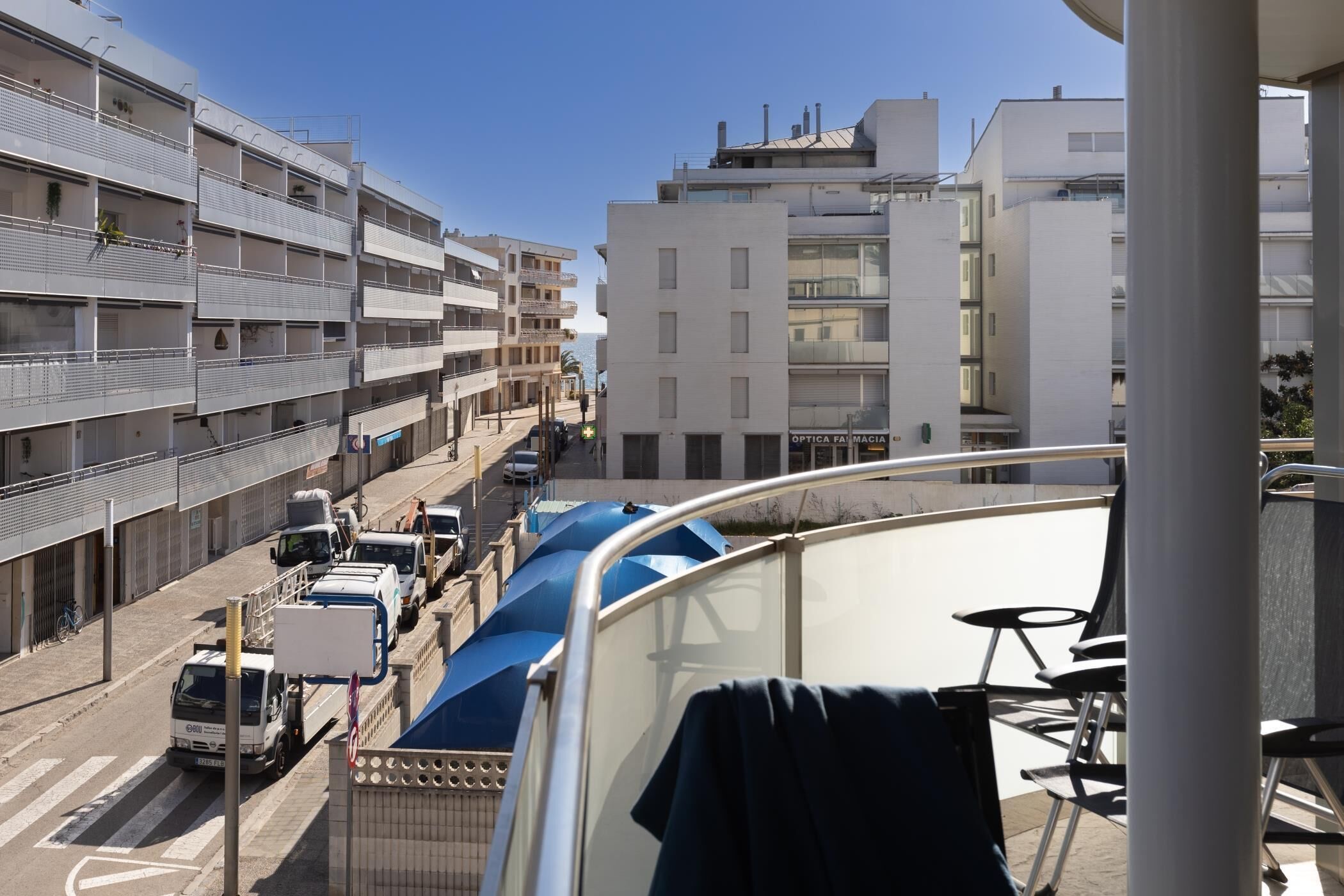 Un edificio de varios pisos con balcones, una calle con vehículos estacionados y un cielo despejado.