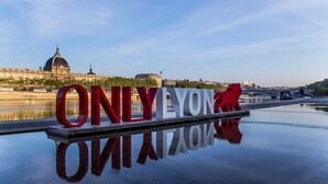 Une pancarte sur laquelle on peut lire en grandes lettres « UNIQUEMENT LION », se reflétant sur une étendue d’eau calme, avec une vue sur la ville en arrière-plan.